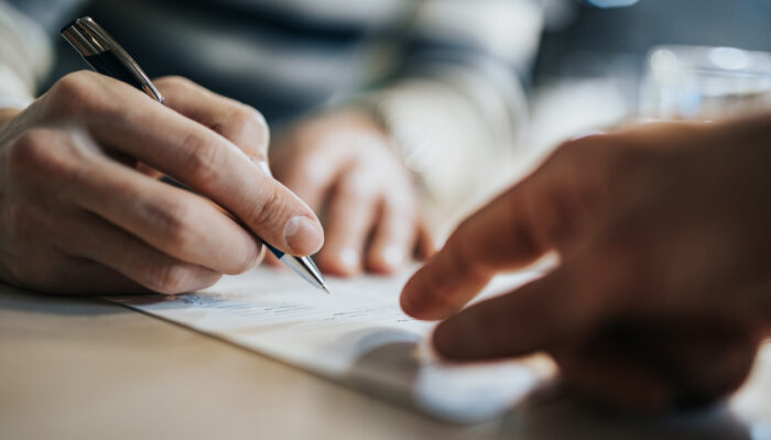 Close up of unrecognizable man signing a contract while financial advisor is aiming at the place he need to sign.
